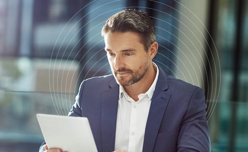 A man in a blue suit reads a tablet intently, with a blurred modern office background. Concentric rings faintly surround him, suggesting focus.