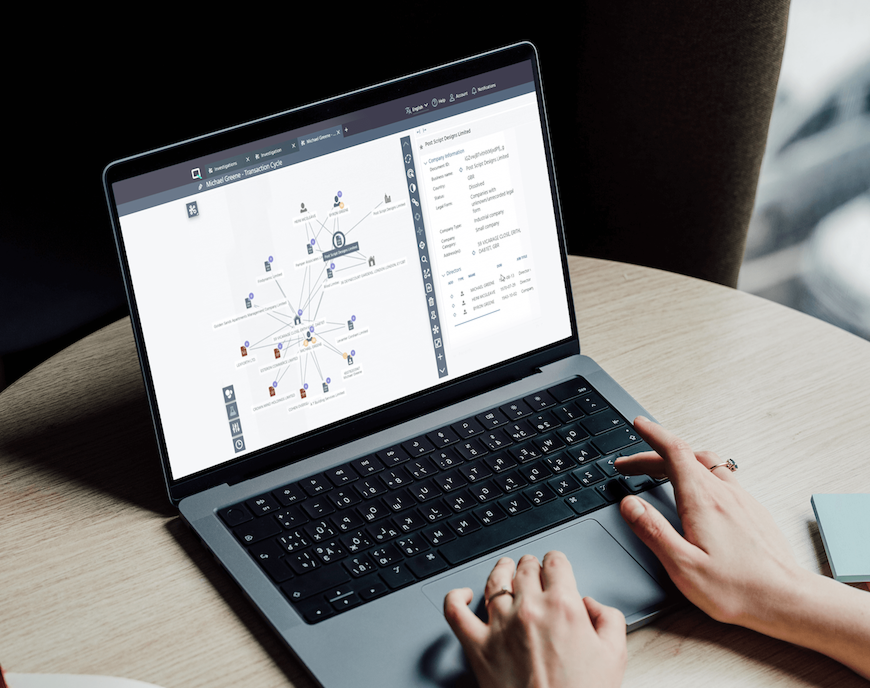 Person using a laptop displaying a network diagram and data analysis on the screen, with hands on the keyboard, on a wooden table.